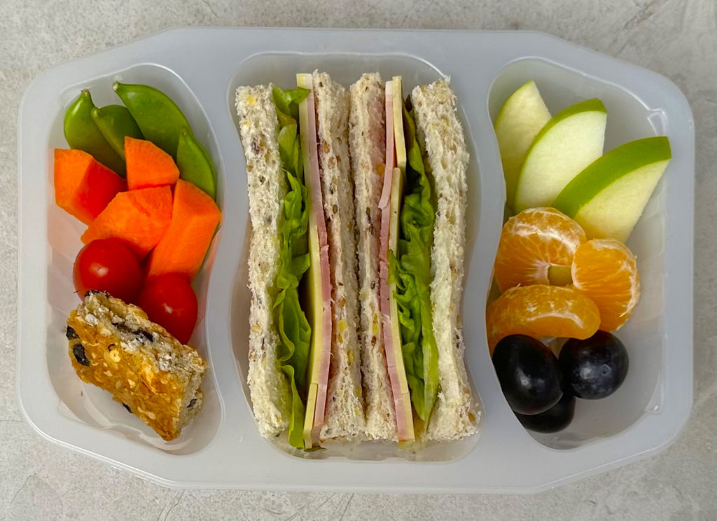 Bento style lunch pack with ham, cheese & lettuce sandwich, veggie sticks, oat slice and fruit